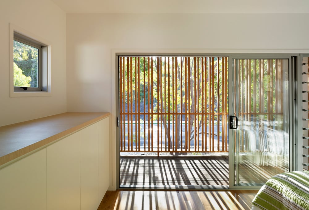 主卧室通过通高滑动玻璃通往半私密阳台，天然木条在空间中投下交错的阴影。