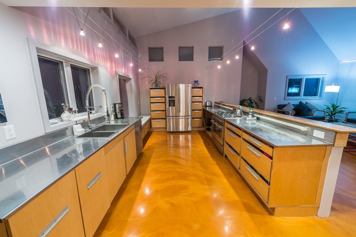 两组轨道照明装置悬挂在厨房台面上方的墙壁和天花板上。不锈钢台面和固定装置排列在这个宽敞的厨房两侧。