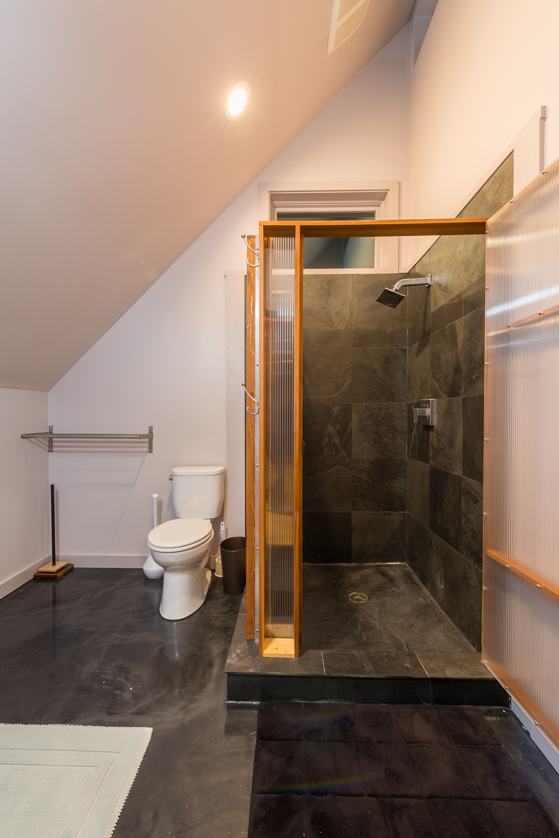 两间卧室共用一间浴室，浴室里有一间深色瓷砖的淋浴间，浴室里有磨砂玻璃和光滑的灰色地板。