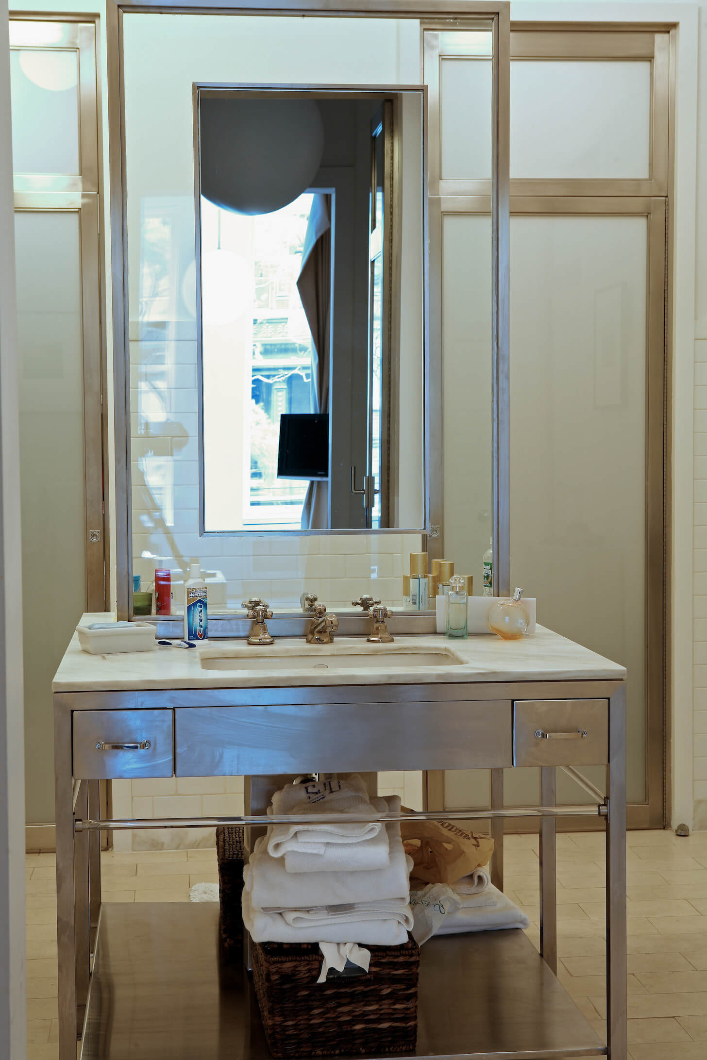 浴室设有一个独立的钢制梳妆台，带有独特的镜子功能，镜框在玻璃中。奶油色地砖与大理石台面相配。