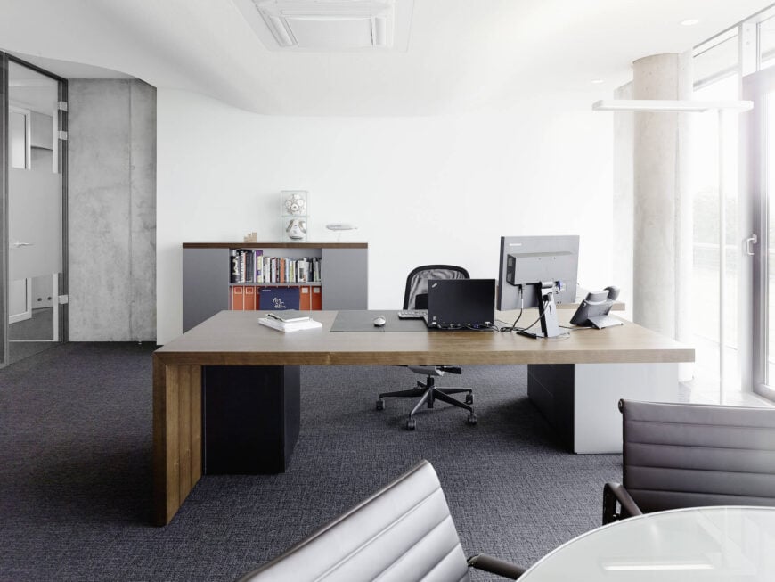 最后，我们留给你的是一间独特的办公室，里面有一张极简主义的天然木桌，上面铺着灰色地毯，上面有起伏的天花板，右边是全高的外部玻璃。