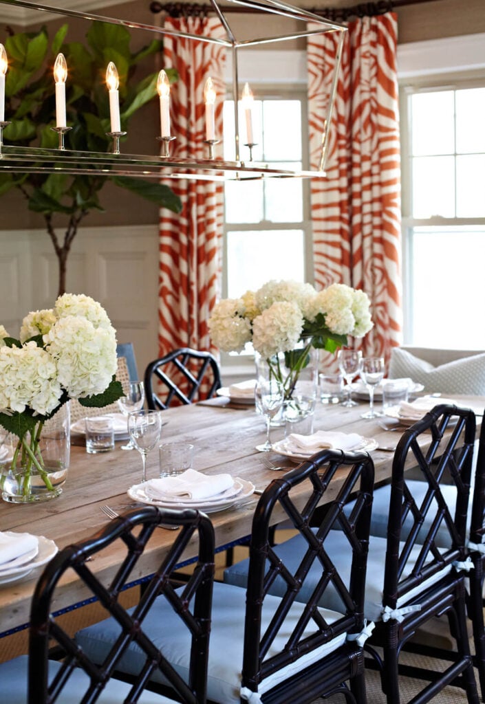 光滑、干净的玻璃器皿线条增强了天然木桌的乡村魅力。桌子上有两个摆放整齐的白色绣球花的中心装饰品。