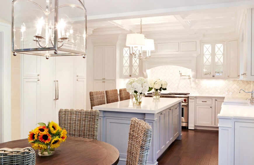 白色的u形厨房在厨房岛上有配套的柳条凳子和可爱的奶油瓷砖后挡板。
