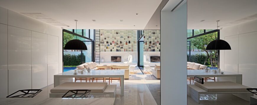 宽敞的开放式设计客厅区有一个巨大的两层书架，靠在远处的墙上，周围摆放着定制的白色现代家具。