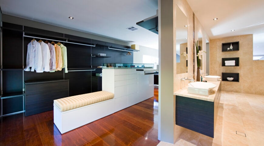 浴室让位给一个宽敞的步入式衣柜空间。深色的木墙置物架与中间的白色岛状置物架形成对比，上面是与客厅相同的丰富硬木地板。