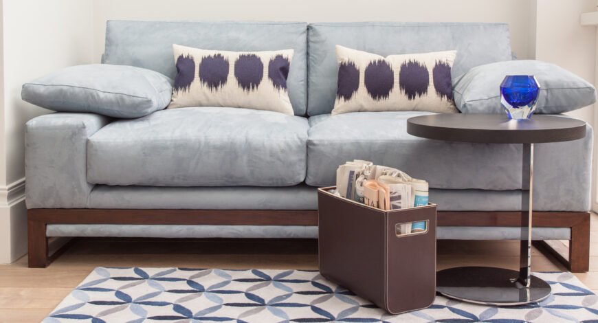 这款独特的沙发设计以天蓝色的内饰为特色，采用了现代木架，并配有超厚的缓冲。一张圆形的现代木制和金属桌子放在蓝色和白色图案的地毯上。