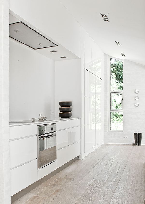 全高的白色极简主义橱柜位于厨房旁边，连接到一面墙，墙上有三扇窗户，一直延伸到倾斜的天花板。