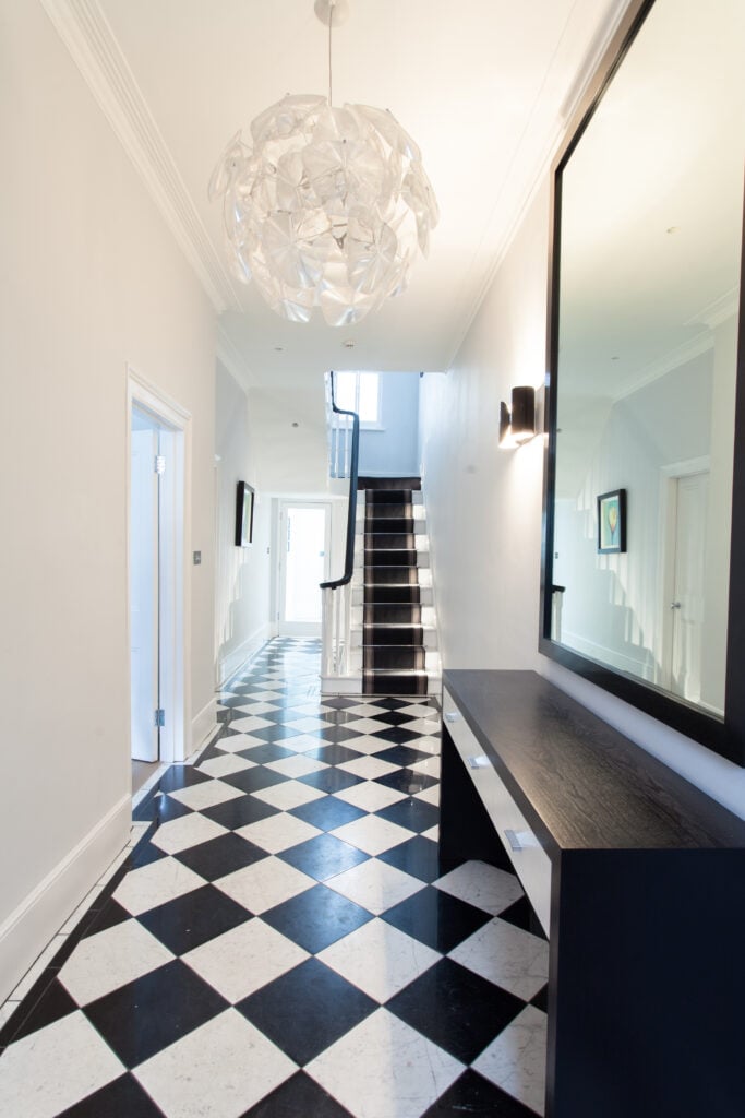 中央走廊以黑白格子瓷砖地板为特色，增加了一种俏皮的感觉，与这里看到的极简主义的边桌和楼梯相匹配。另一个球形吊灯，花卉形状，出现在这个空间。