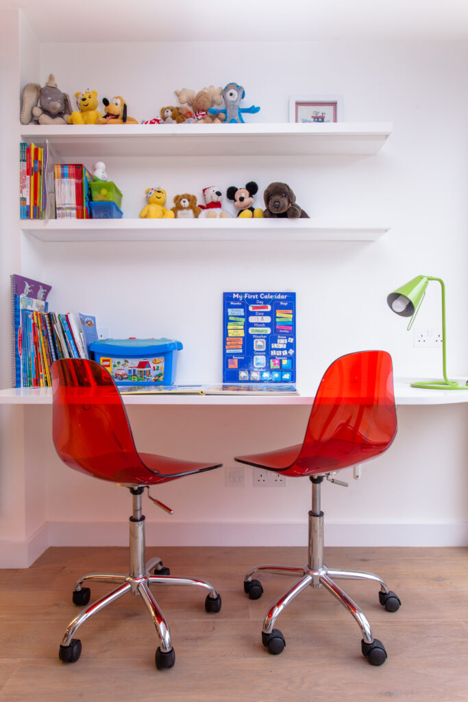 游戏室是这个家庭中各种色彩萌芽的地方。在这里，一对红色丙烯酸座椅位于内置书桌和白色书架下面。
