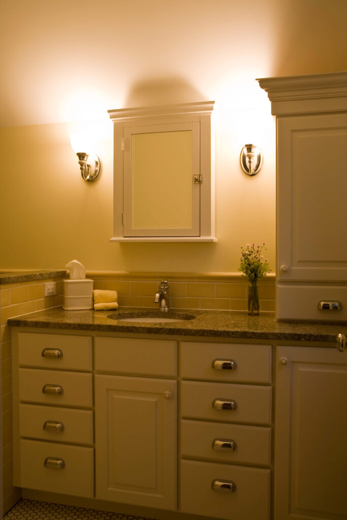 浴室里有花岗岩台面和白色橱柜，配有镀铬五金，周围环绕着一面独特的白木镜框镜子。