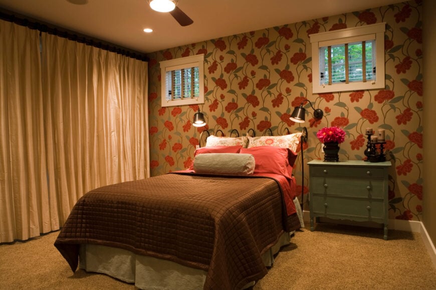主卧室充满了丰富的色调，包括远端大胆的花卉壁纸。棕色和红色的床单与主题相匹配，米色的地毯。