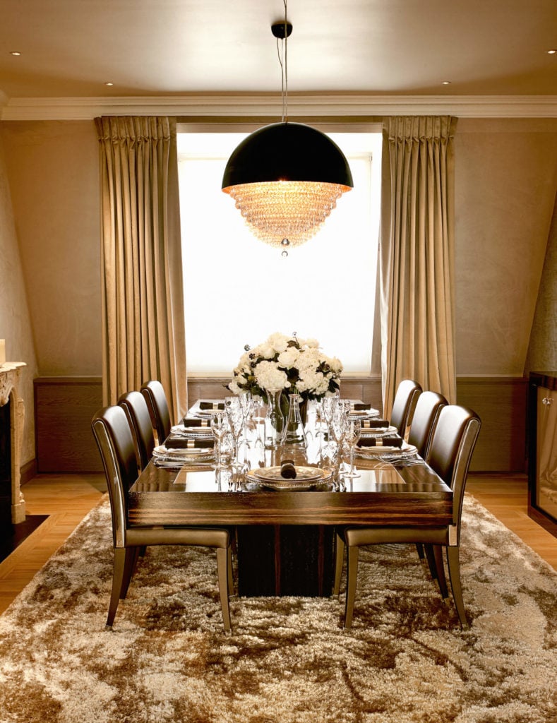 餐厅拥有这张特厚的木质餐桌，搭配一套皮革软垫侧椅，在一个独特的吊灯下，结合了球形的身体和传统的水晶结构。金色的窗帘突出了房间的丰富色调。