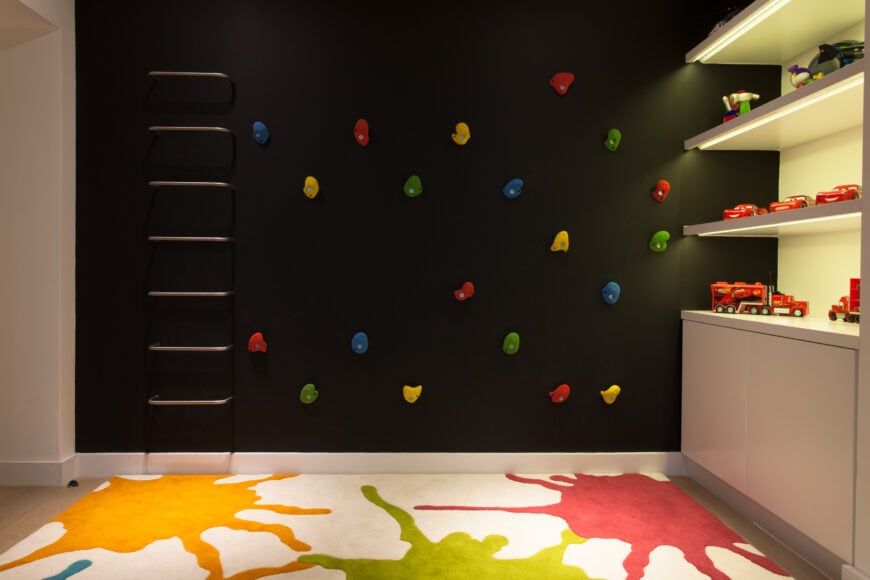 儿童空间的远端有一面黑色的攀岩墙，旁边是优雅的、内部照明的玩具收藏架。飞溅的油漆地毯统一的外观。