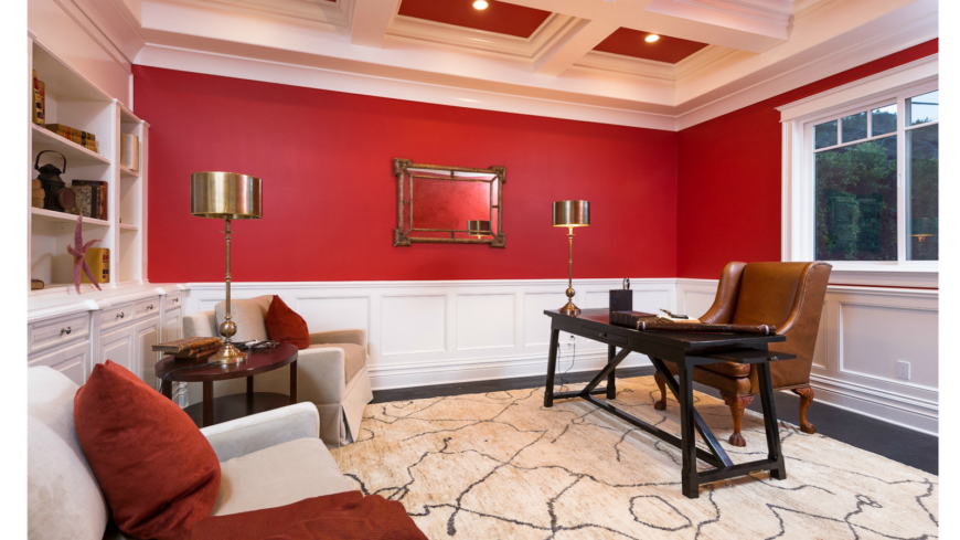 家庭办公室与家中更多的公共房间不同，墙壁和天花板上涂着明亮的红色油漆。定制的格子天花板很优雅，与较低墙壁上的白色护壁板和内置书架相匹配。