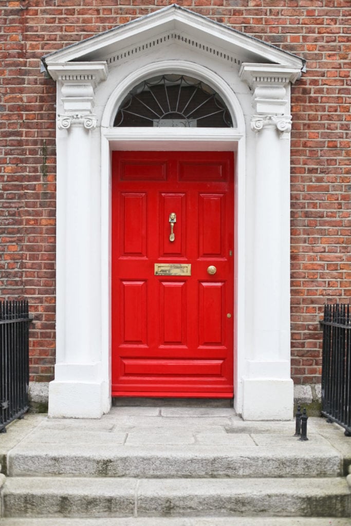 白色的拱形门框和半圆形的横梁使这扇红色的门从更柔和的砖块和浅灰色石阶中脱颖而出。