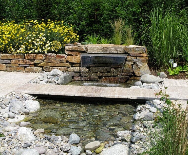 一个由嵌在石头边缘的瀑布喷泉供养的浅池塘。一条狭窄的石桥连接着小路的两边。