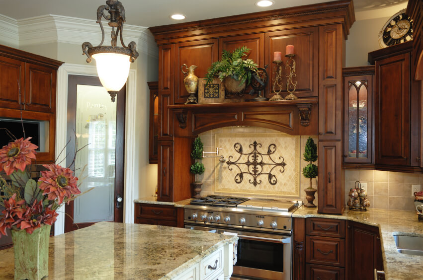 一间旧世界风格的深色木质厨房，配有浅色大理石台面和米色石材后挡板。炉子上方的中心布置在中间有一个装饰性的铁设计。