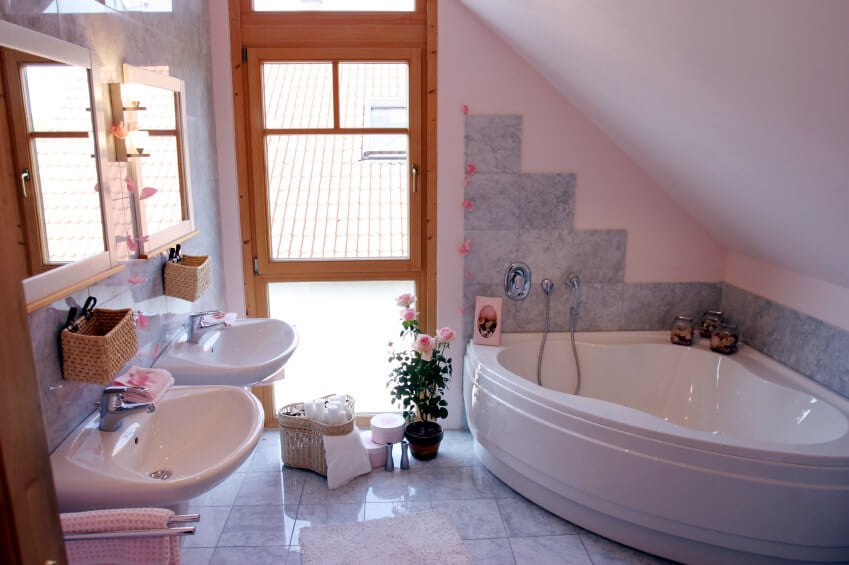 一个非常女性化的浴室，浅灰色和粉红色的瓷砖。淡粉色的墙壁与玫瑰和粉红色的毛巾相搭配。每个壁挂式水槽都有自己的镜子。