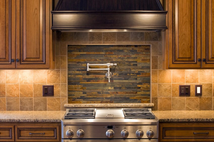 这是一间漂亮的棕色厨房，后挡板是石头砌的，中间镶嵌着细长的木炭和青铜瓷砖。