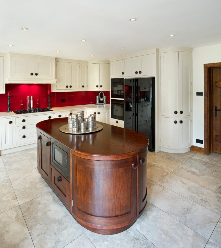 白色的厨房，有圆形的橱柜和椭圆形的厨房岛台，用的是深色的硬木。令人惊叹的深红色后挡板立即吸引眼球。