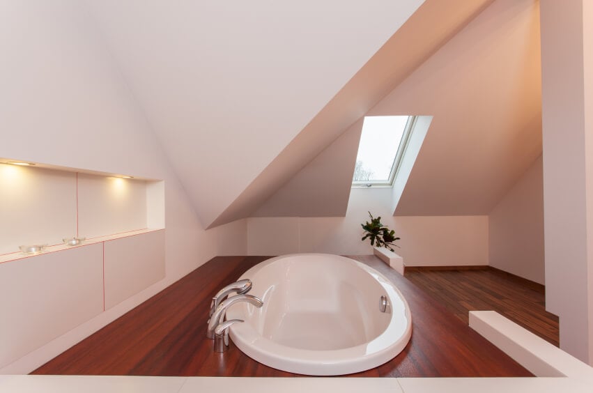 一间令人放松的极简主义浴室，设有内置搁架，浴缸嵌在比主楼层更高一层的木质围栏内。