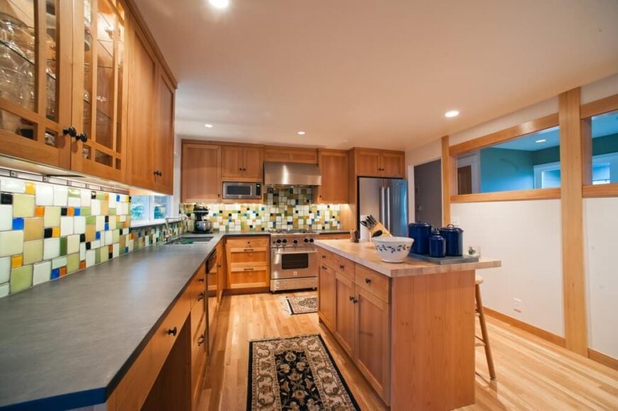 一个木质厨房，有一个大胆的、彩色的、有点滑稽的后挡板，用不同大小的彩色瓷砖制成。