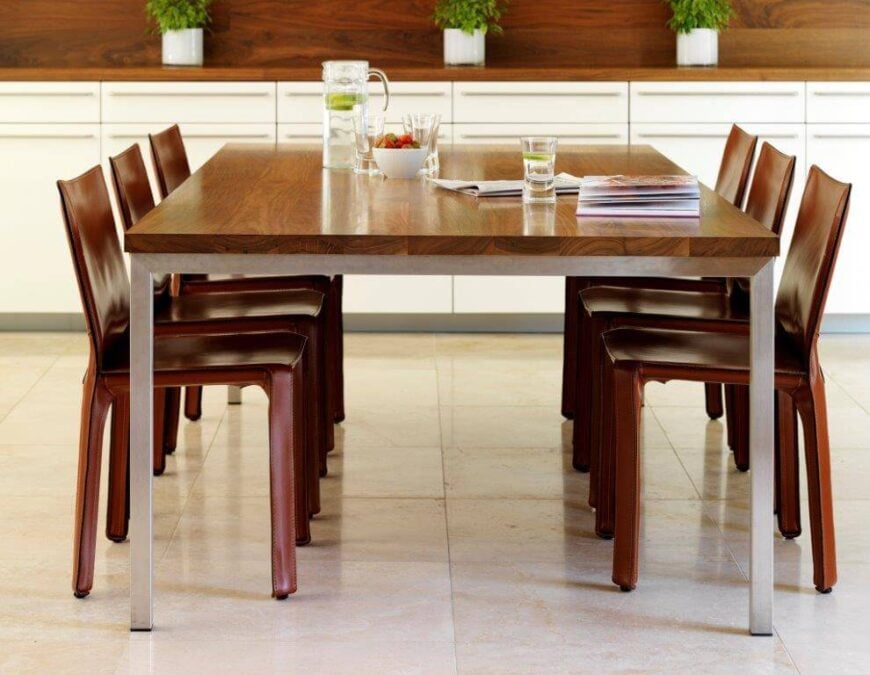 硬木早餐桌的桌腿比桌顶更轻，细长的餐椅的色调要暗得多。桌子后面的墙上是一个长长的木制台面，上面和下面都有橱柜。台面上放着几盆药草。