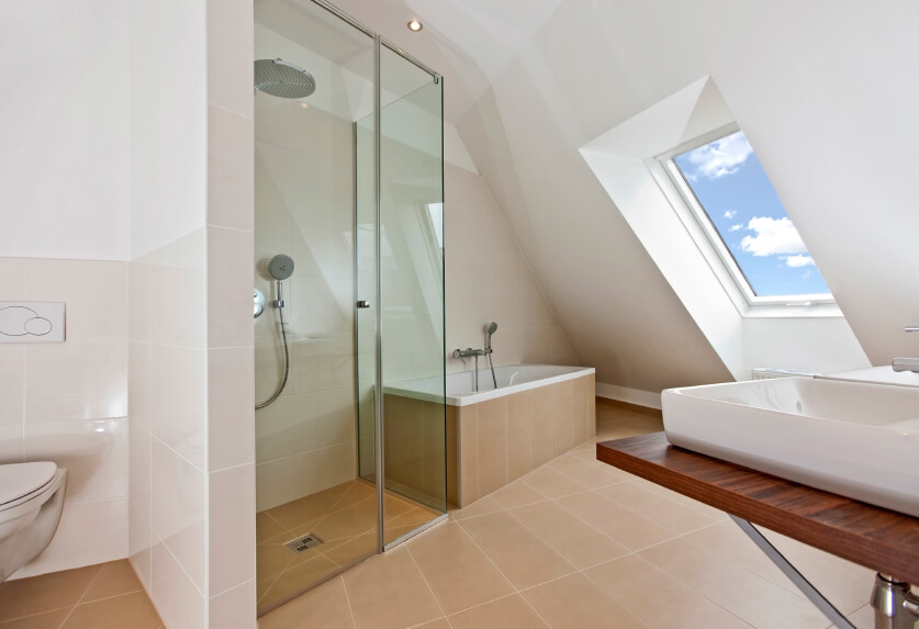 阁楼浴室有一个奇妙的天窗和充足的空间。容器水槽放置在木制和镀铬的极简主义梳妆台上。玻璃淋浴间紧挨着深而豪华的浴缸，浴缸铺着暖色调的地砖。一面小墙有助于为厕所提供一些隐私。