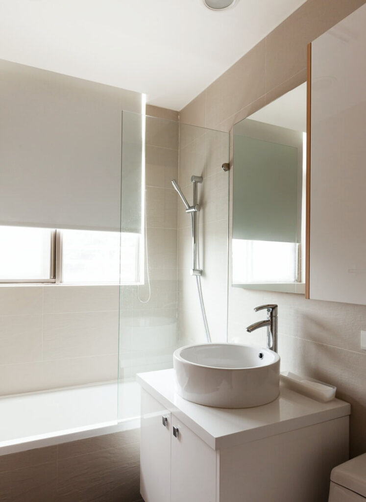 这间大小适中的浴室有一个深水槽和一个带有镀铬固定装置的淋浴浴缸组合。浴缸外面铺着米黄色的纹理瓷砖。