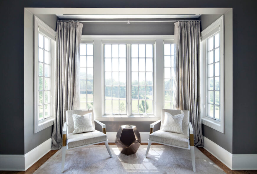 主套房飘窗边的一个小休息区。当代风格的椅子与小地毯和青铜金属边桌相匹配。座位区后面微妙的条纹窗帘增加了图案的维度。
