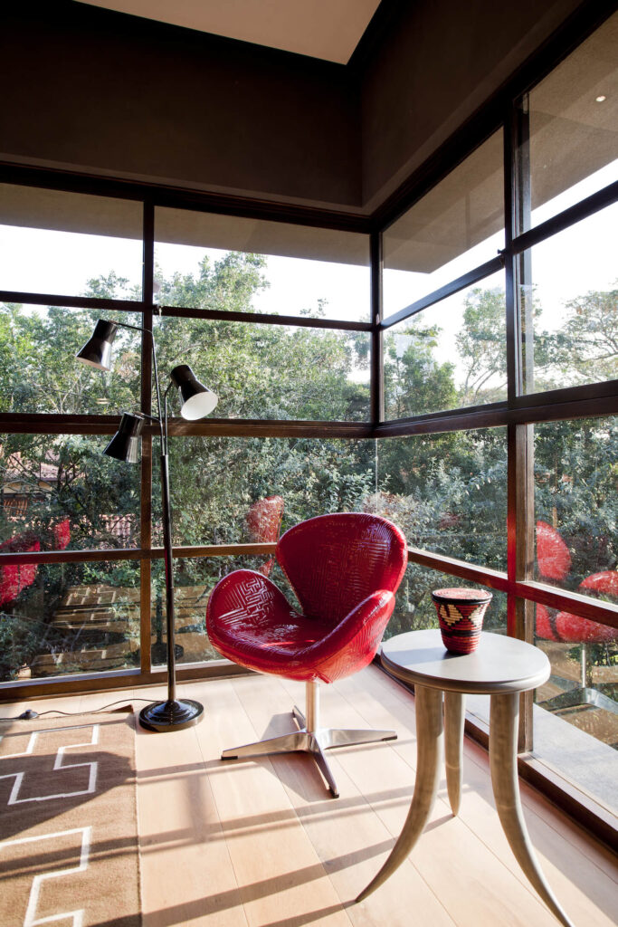 这个安静的角落空间里有一张小桌子和明亮的红色扶手椅，坐在落地窗提供的阳光下。