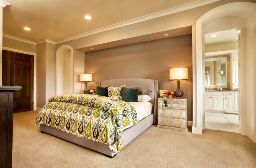 主卧室采用了淡中性色调，但绿色和蓝绿色孔雀印花床罩和抱枕使空间更加明亮。床头柜前面有一个圆形图案的镜面。