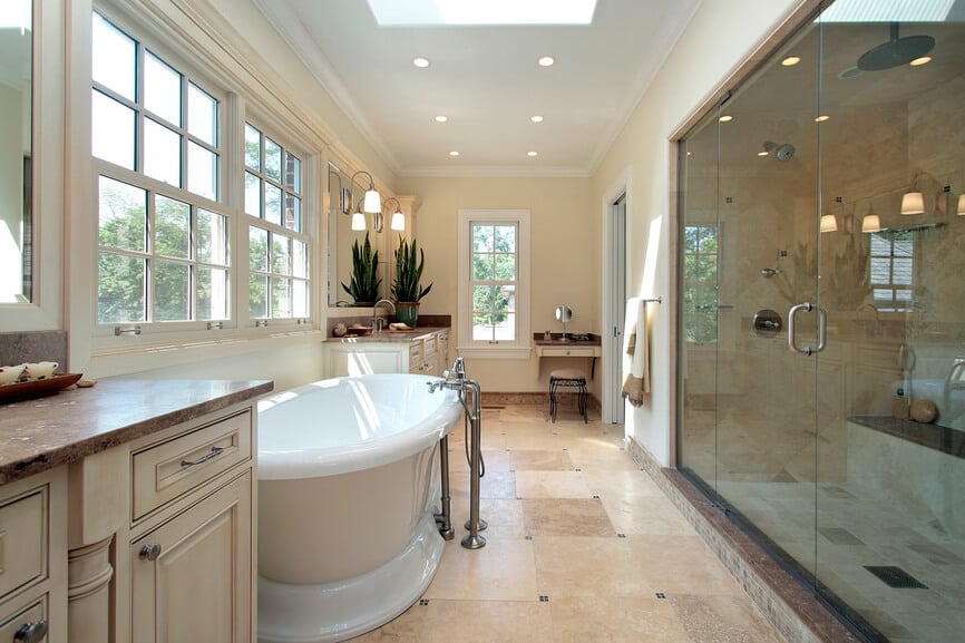 这个令人印象深刻的浴室提供了足够的空间。一个深瓷浴缸拥有不锈钢龙头和管道，而一个相当大的玻璃封闭淋浴附近。嵌壁式照明装置安装在顶部成型的白色天花板上，天窗补充了大量的窗户，使光线能够渗透进来。石材地砖与墙壁和双梳妆台的柔和中性完美互补。