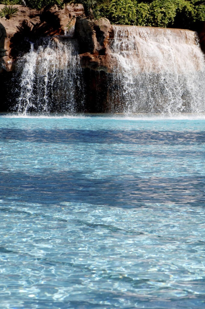 一个人工瀑布翻滚到游泳池里。水和人造石的流动被设计成与自然瀑布尽可能多的流动和外观。