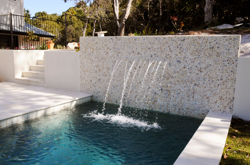 一个石头和砂浆墙在一个泳池边缘，几个喷泉从水平裂缝流入狭窄的长池。