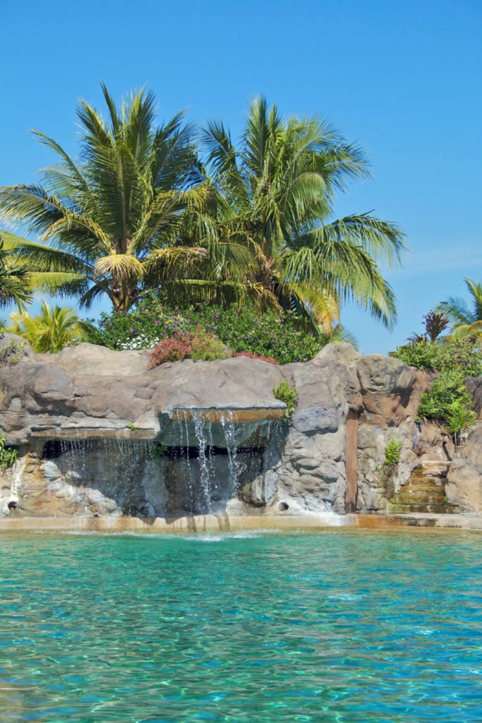 一个大型人造石头露头沿着这个宽敞的游泳池的边缘，几个壁架滴入游泳池。