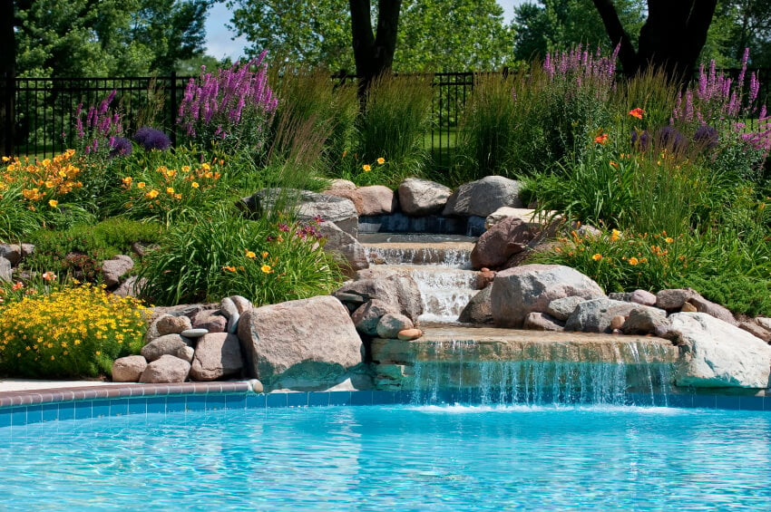 一个美丽的石头瀑布，水池周围是萱草和其他美丽的开花灌木。