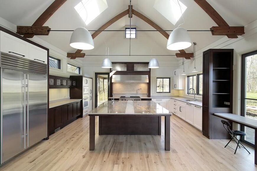 在这里，我们有一个完全现代化的厨房，配有拱形天花板，在中央一个巨大的玻璃顶岛面上露出深色木梁。一对天窗位于天花板的两侧，深色的天然木橱柜和浅色的硬木地板增添了丰富的质感。