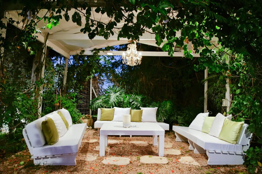 这个华丽宁静的花园露台位于铁结构下。简单的白色长椅上覆盖着白色靠垫和绿色靠枕。一盏小吊灯增添了一种令人难以置信的优雅感。