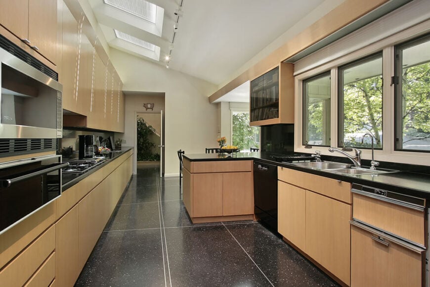这个光滑的现代厨房以深色大面积瓷砖地板和浅色木橱柜为特色，在倾斜天花板上的一系列大天窗下自然采光。这种对比在这个空间中产生了一种新的效果。