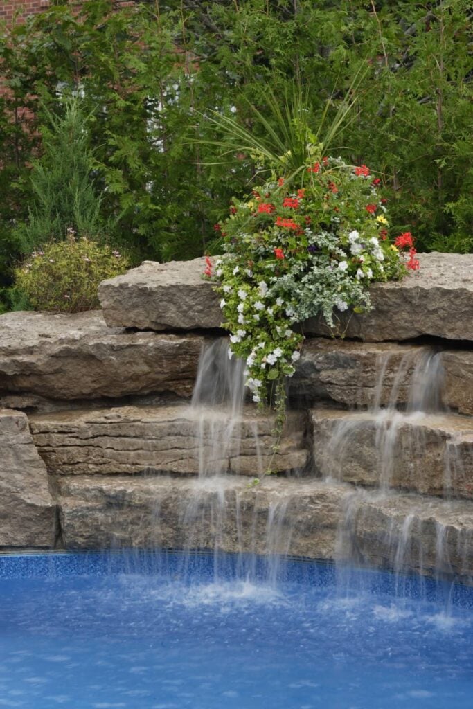一个整齐地安排的人工瀑布，将级联进入地面泳池。顶部石头上的花朵安排与水和谐地覆盖着。