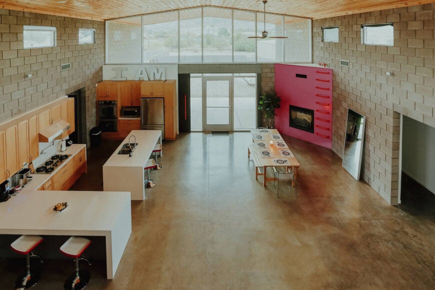 从上面看，住宅的前半部分是一个空旷的开放空间，有着独特的细节，包括木制餐桌和粉红色的壁炉结构，阳光透过宽阔的大窗户照射进来。