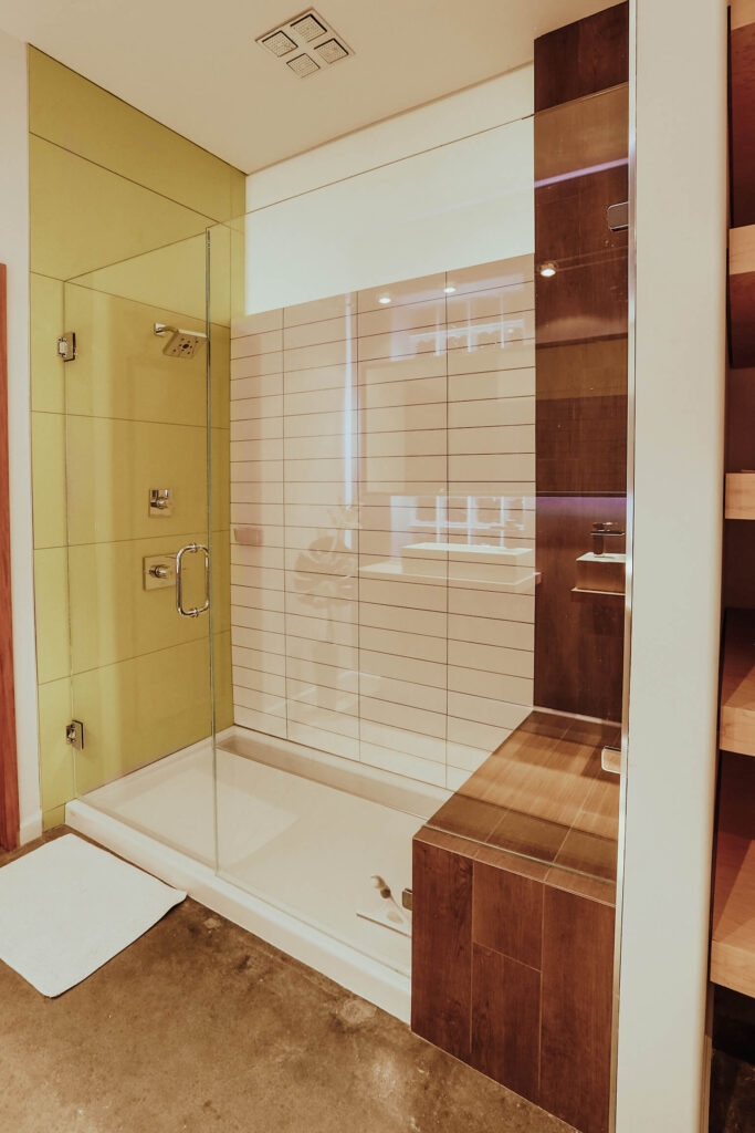 玻璃封闭的步入式淋浴间拥有三种纹理细节:丰富的天然木材，白色砖瓦和大幅黄色瓷砖。