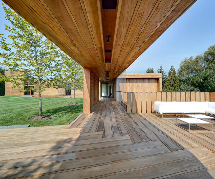 广阔的木板路以复杂的木板设计为特色，支撑着各种有用的空间。在这里，我们看到一个充满阳光的放松区，白色软垫，金属框架露台家具。