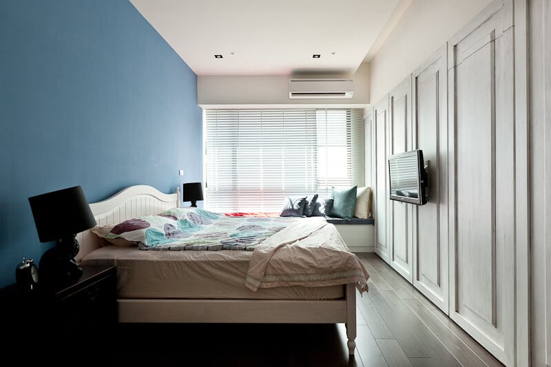 主卧室的特色是深色硬木地板，白色的墙长面板，木架床后面有一面大胆的蓝色墙壁。通高的窗户使自然光贯穿始终。