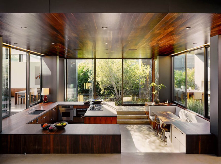厨房内的高平面俯瞰整个空间，由台面和书架垂直划分，书架是早餐角。天花板反映了丰富的木材色调。