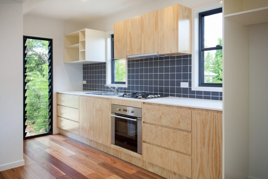 浅色的橱柜与丰富的硬木地板形成对比，而深色的后挡板瓷砖将厨房与其余的开放区域隔开。