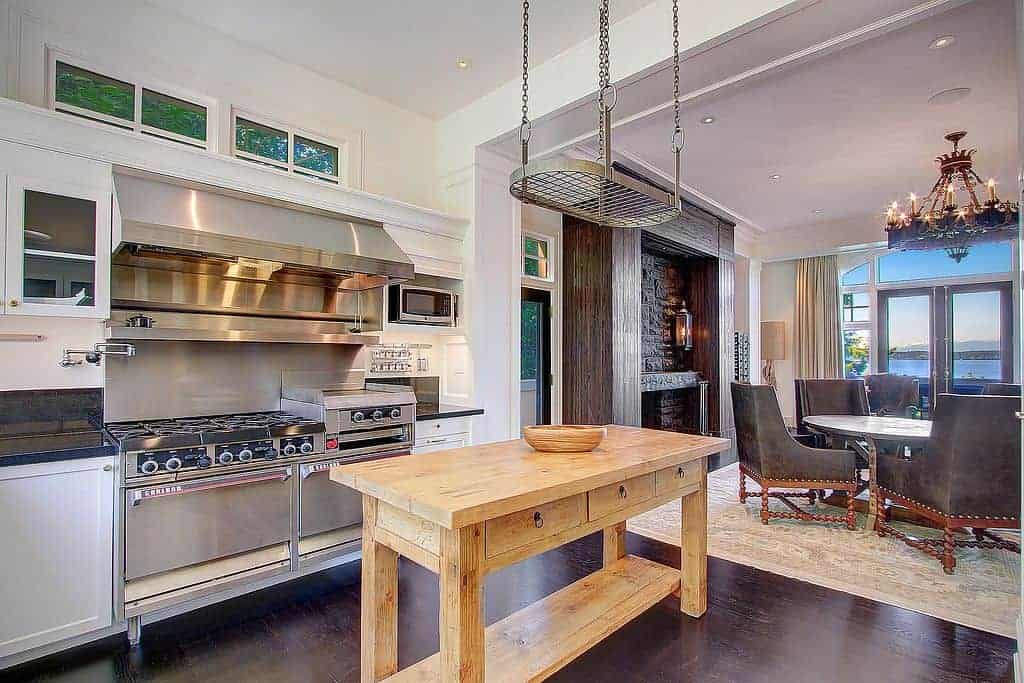 农舍厨房的另一个角度，配有不锈钢用具，木制餐桌厨房岛岛上方的空悬挂potrack，以及深色木地板。