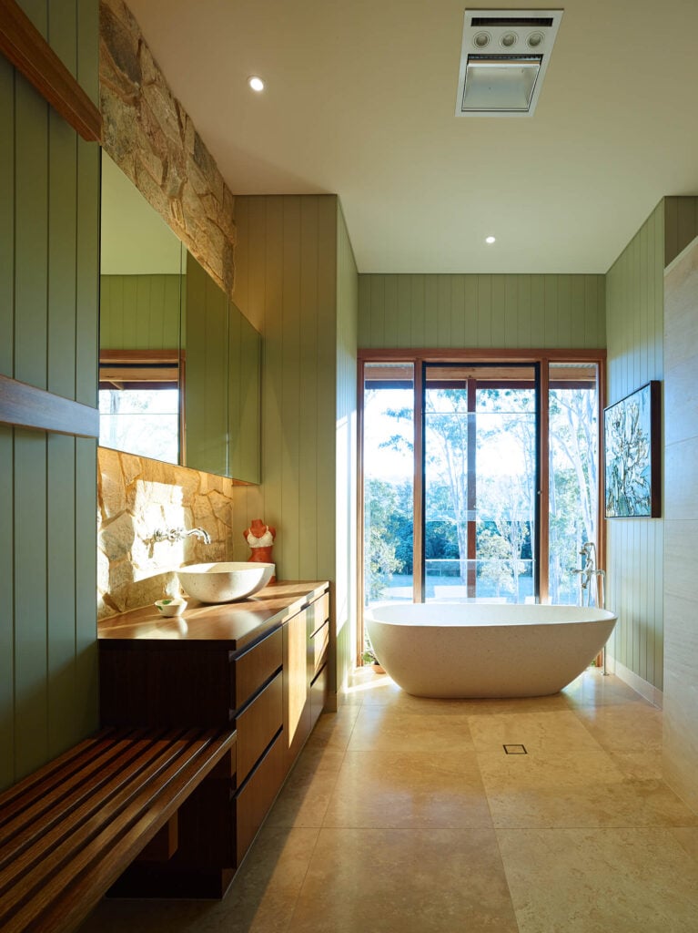 浴室设有全高窗户下的大型底座浴缸，位于大面积瓷砖地板上。丰富的木材梳妆台与容器水槽功能无框镜子安装在石头后挡板。