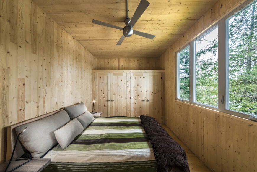 主卧室从上到下都包裹着天然木板，远端有内置的存储空间。床对着一组大窗户，面朝湖。